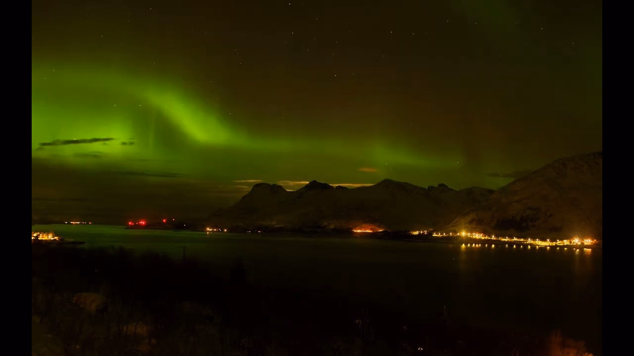 Green aurora over mountains and illuminated shoreline in Svolvær